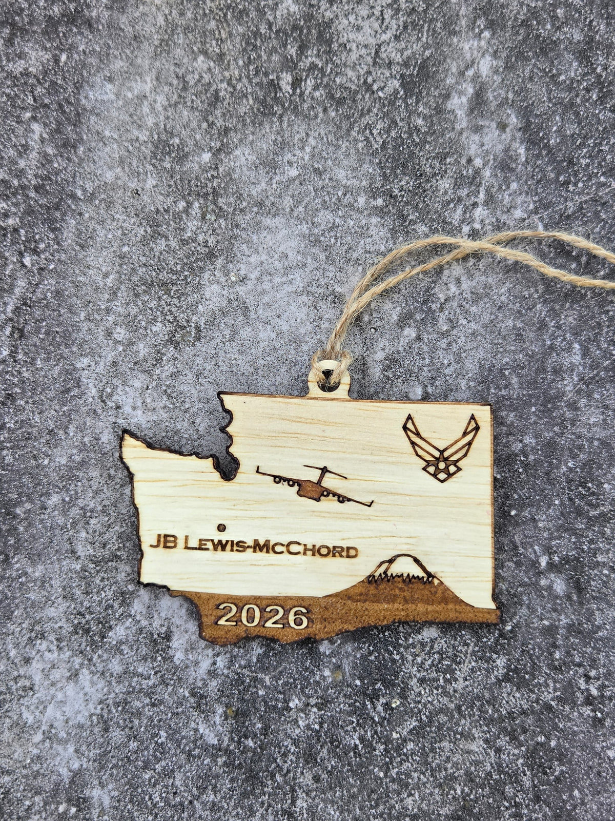 JB Lewis-McChord Washington ornament with its twine loop, lying flat on gray stone