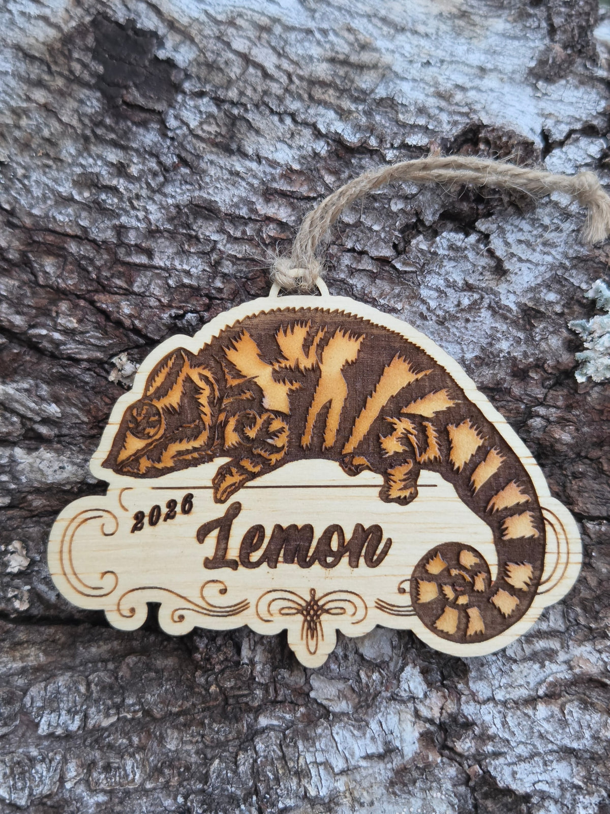 Wooden chameleon ornament, painted, resting along the top of a scrolled plaque with a sample name and year engraved