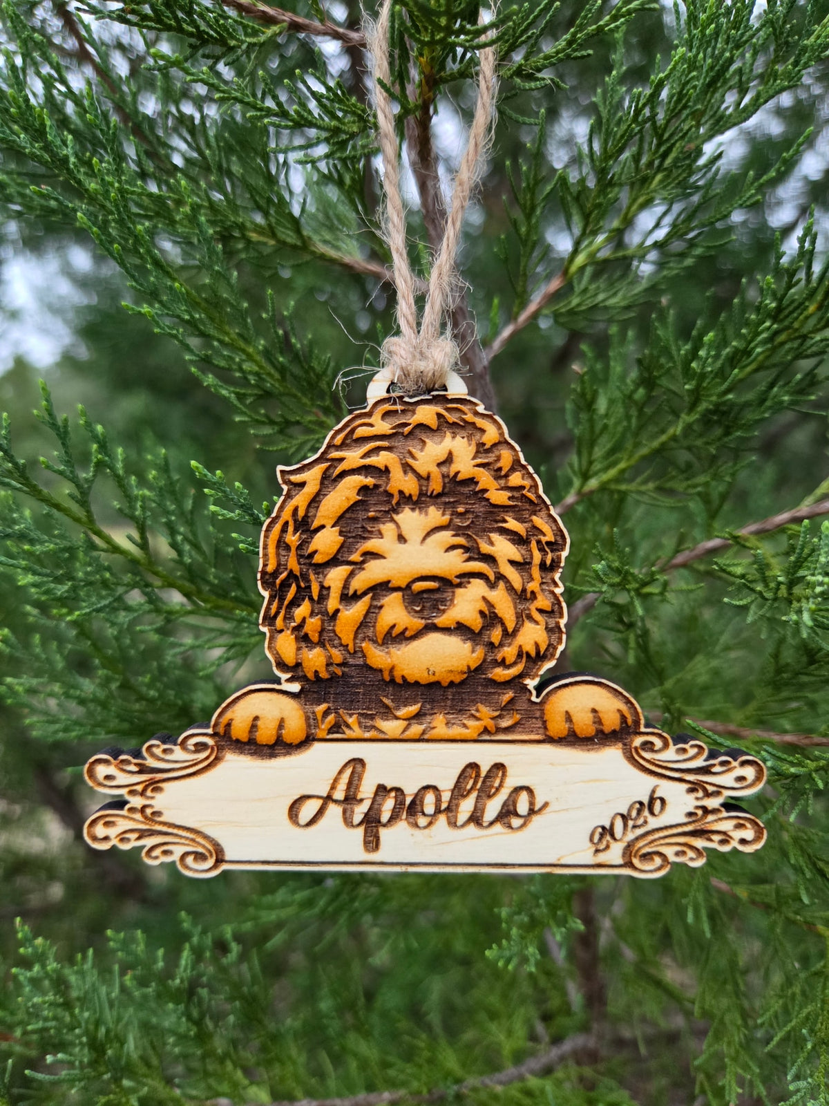 Doodle dog plaque ornament hanging by its twine loop on an evergreen branch