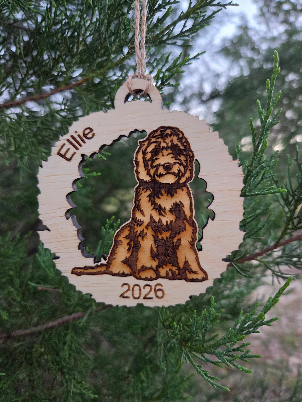 Wooden doodle dog in a wreath ornament, engraved Ellie and 2026, hanging on an evergreen branch