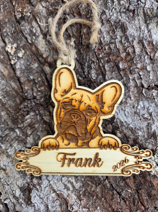 Wooden French Bulldog ornament, ears up over a plaque engraved with a sample name and the year, resting on tree bark