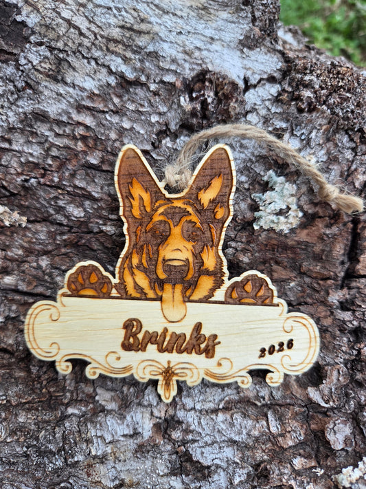 Wooden German Shepherd ornament, ears up over a plaque engraved with a sample name and the year, resting on tree bark