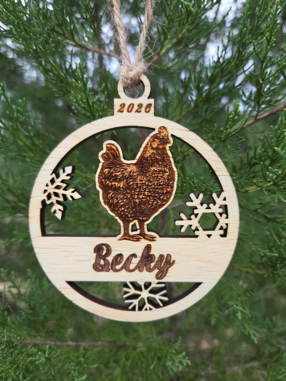Hen and snowflakes ornament hanging by its twine loop on an evergreen branch