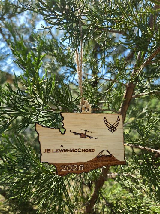 Washington-shaped wooden ornament engraved with JB Lewis-McChord, a C-17A, a mountain and the year, hanging on an evergreen
