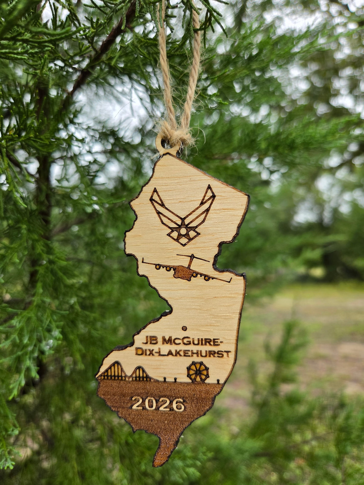 JB McGuire-Dix-Lakehurst ornament hanging by its twine loop on an evergreen branch