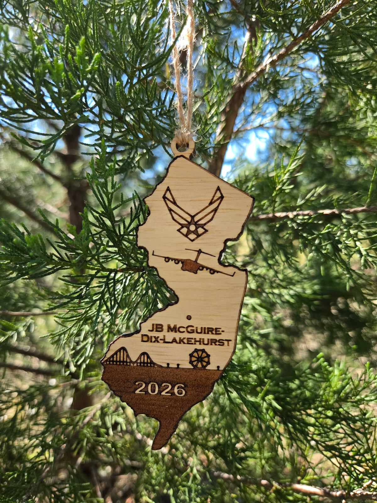 JB McGuire-Dix-Lakehurst ornament hanging by its twine loop on a sunny evergreen