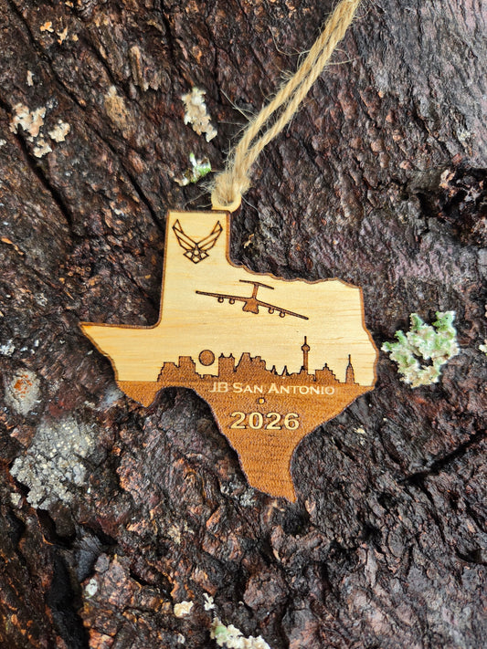 Texas-shaped wooden ornament with a C-5M over the San Antonio skyline, JB San Antonio and the year, resting on tree bark