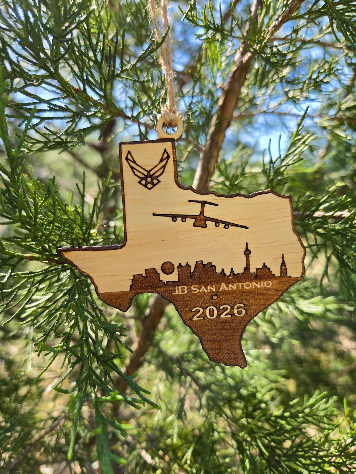 JB San Antonio Texas ornament hanging by its twine loop on an evergreen in the sun