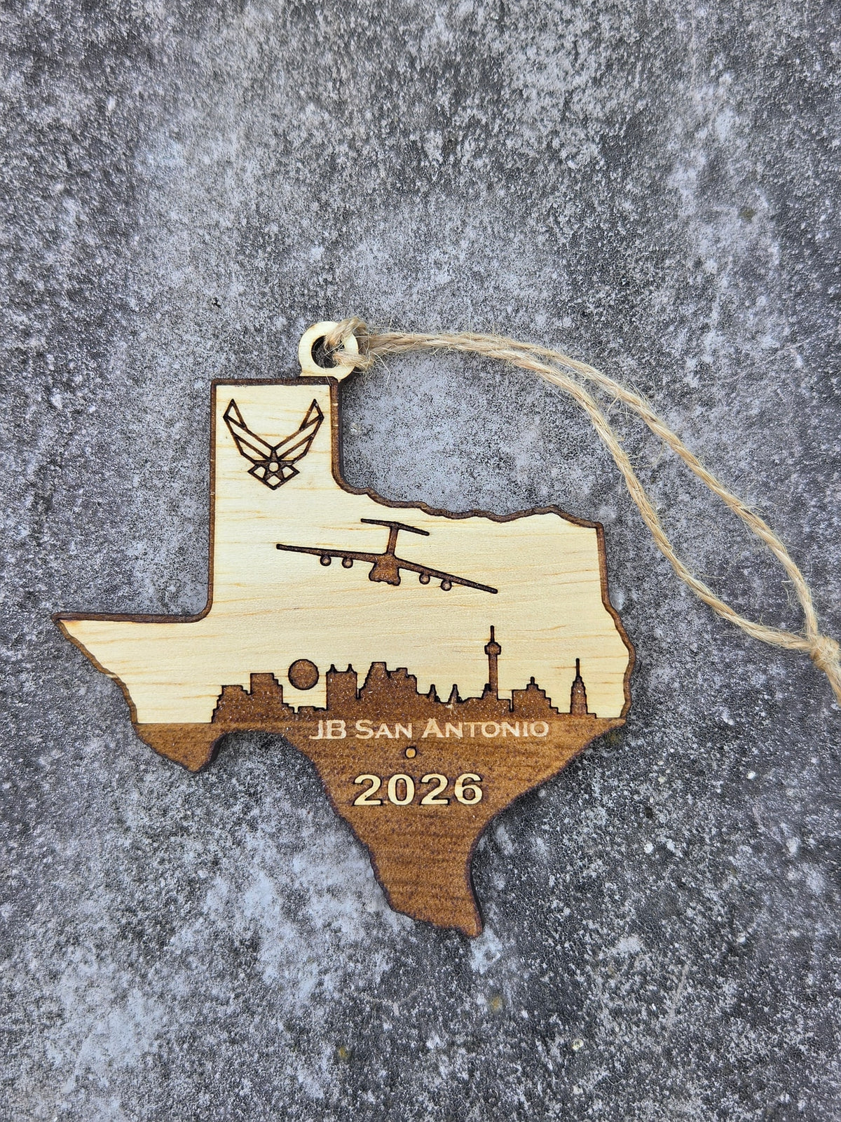JB San Antonio Texas ornament with its twine loop, lying flat on gray stone