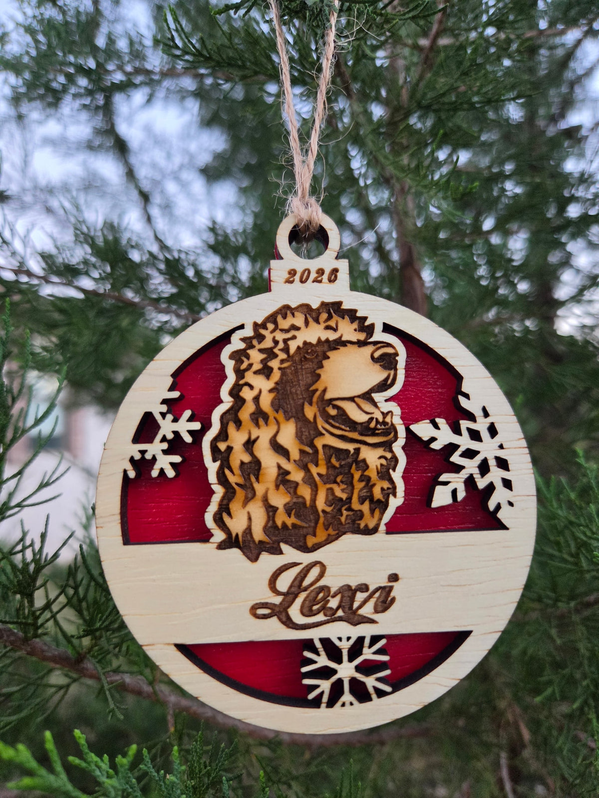The poodle head ornament with a red back, engraved Lexi, hanging on an evergreen