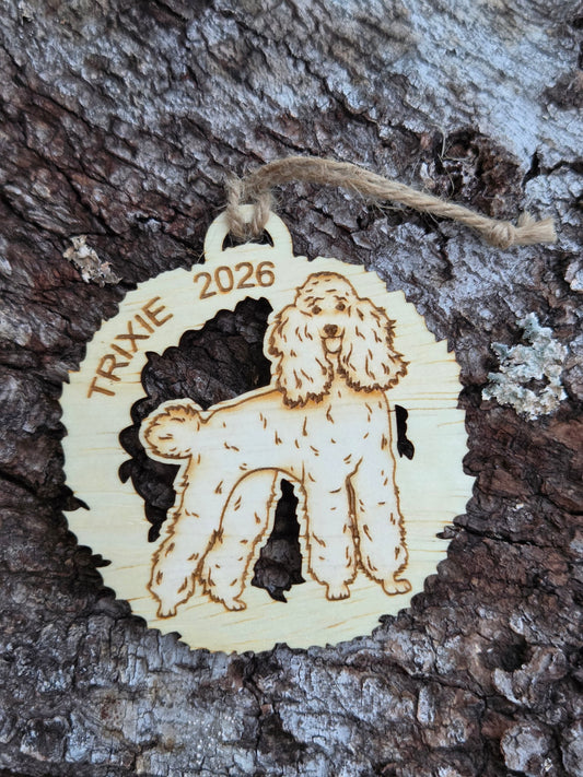Wooden poodle in a wreath ornament with a sample name and year engraved along the top, on tree bark