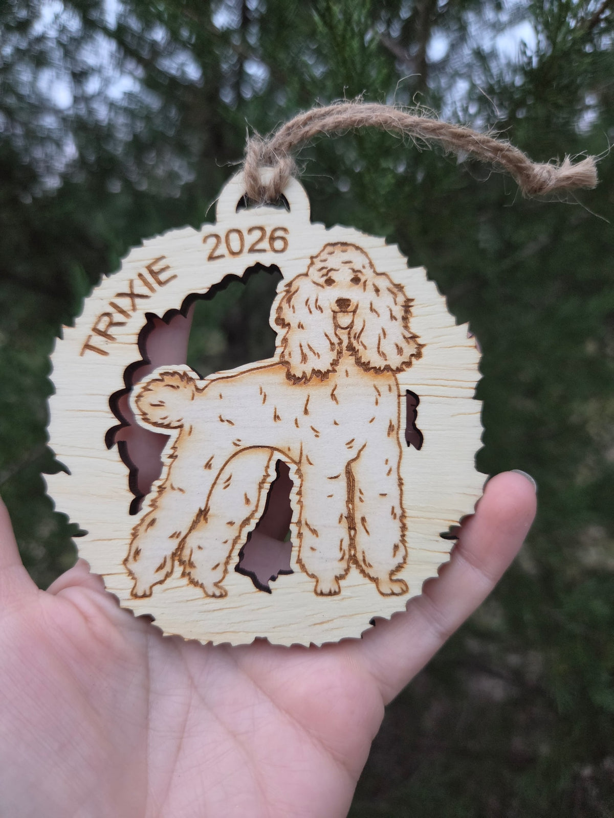 Poodle in a wreath ornament held in an open hand to show its size