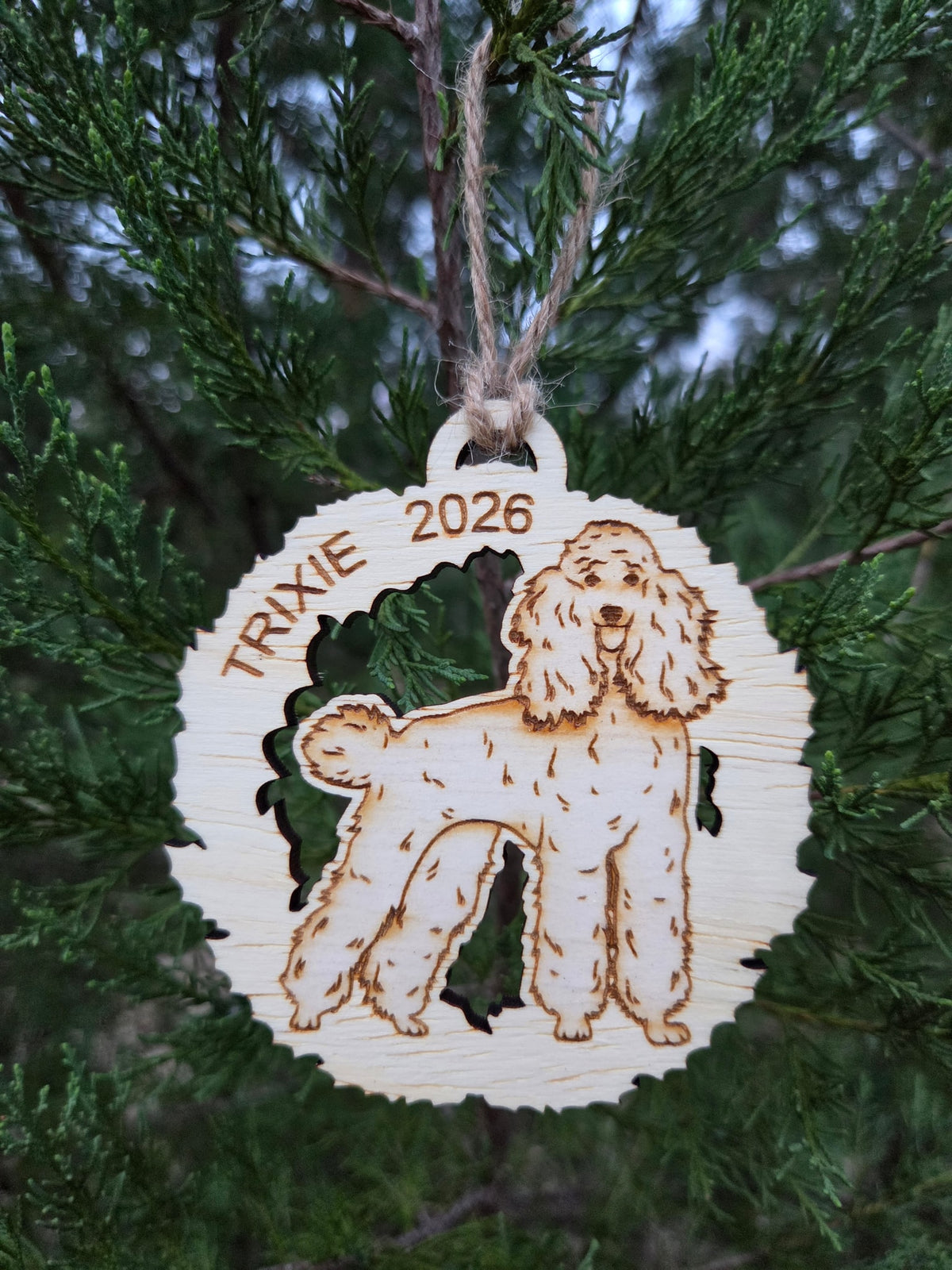 Poodle in a wreath ornament hanging by its twine loop on an evergreen branch