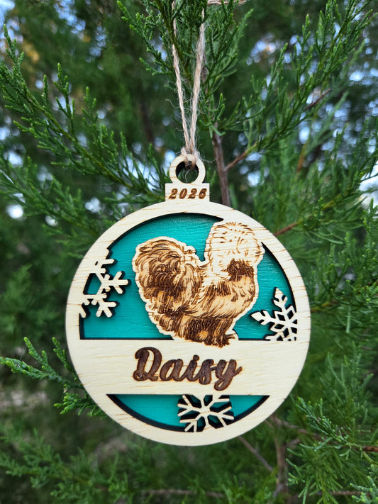 Silkie chicken and snowflakes ornament with a teal back, engraved Daisy and 2026, hanging on an evergreen
