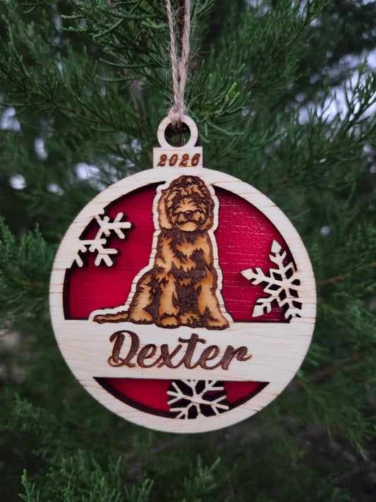 Sitting doodle dog ornament with a red back, engraved Dexter and 2026, hanging on an evergreen