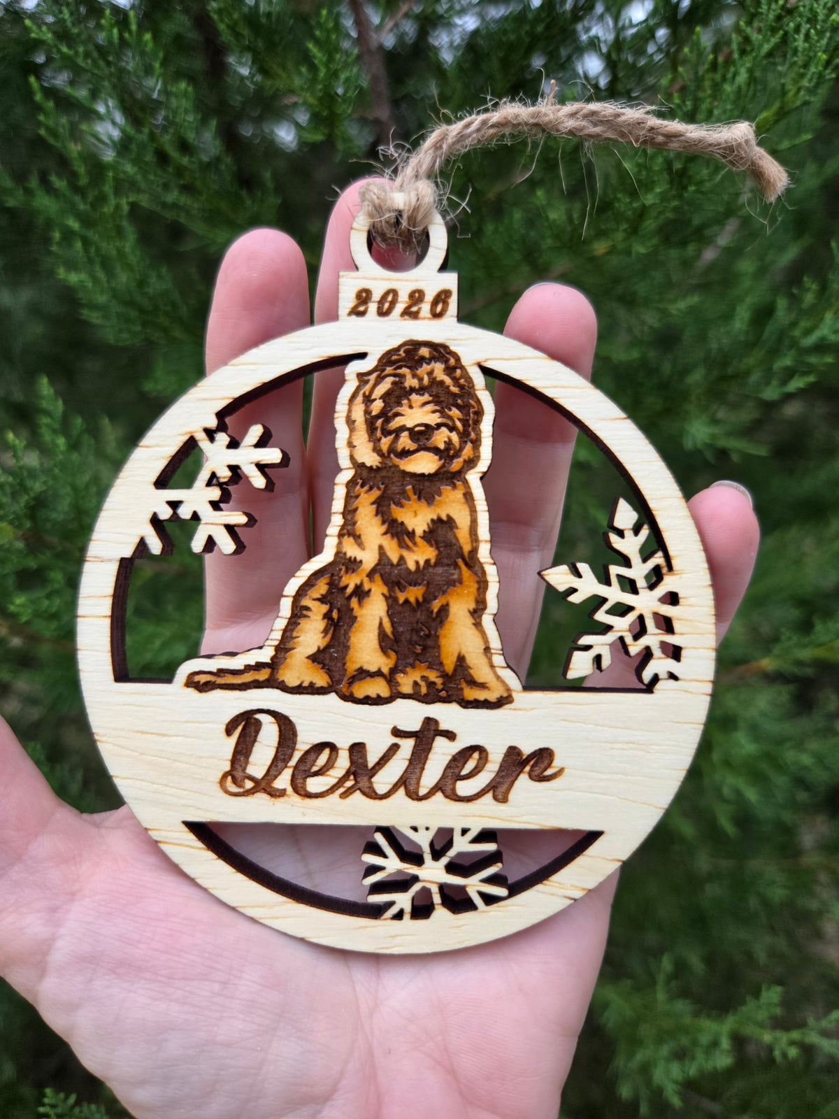 Sitting doodle dog and snowflakes ornament held in an open hand to show its size