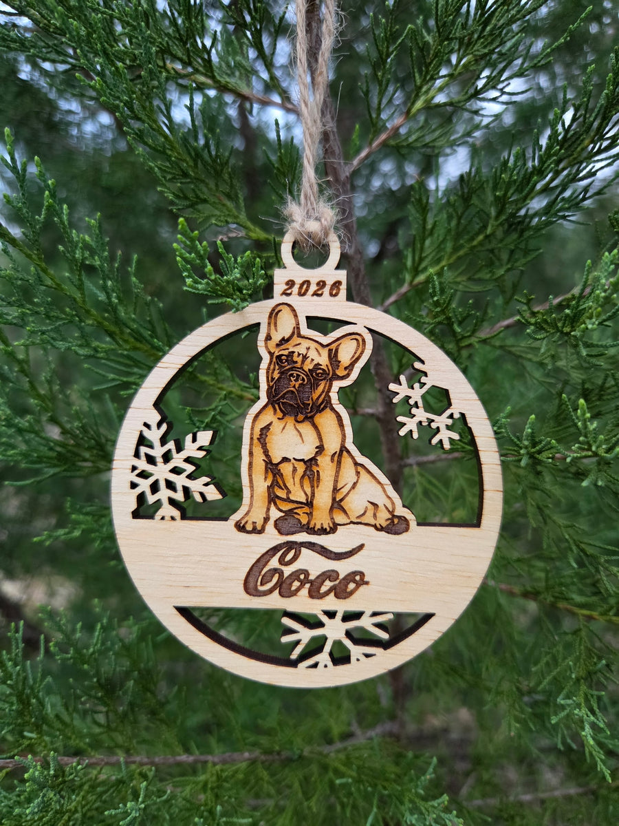 Sitting French Bulldog and snowflakes ornament hanging by its twine loop on an evergreen branch