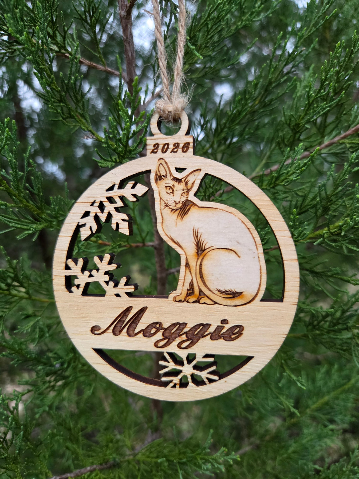 Sitting Sphynx cat ornament hanging by its twine loop on an evergreen branch