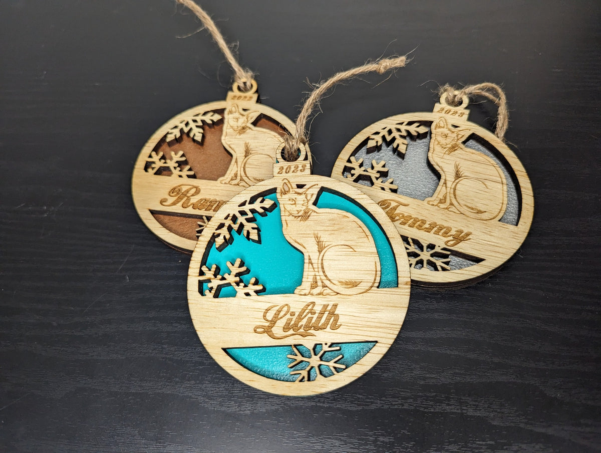 Three sitting Sphynx cat ornaments with copper, teal and silver backs.