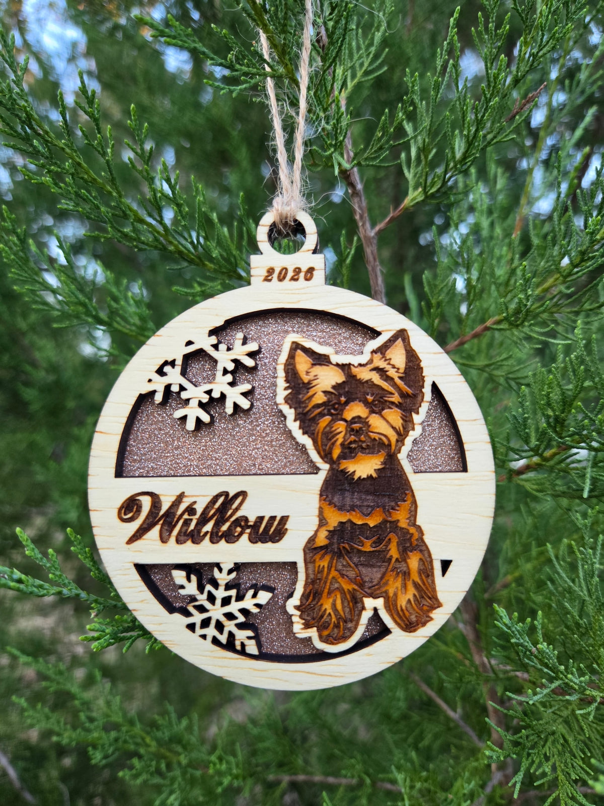 Yorkie and snowflakes ornament with a rose gold glitter back, engraved Willow and 2026, hanging on an evergreen