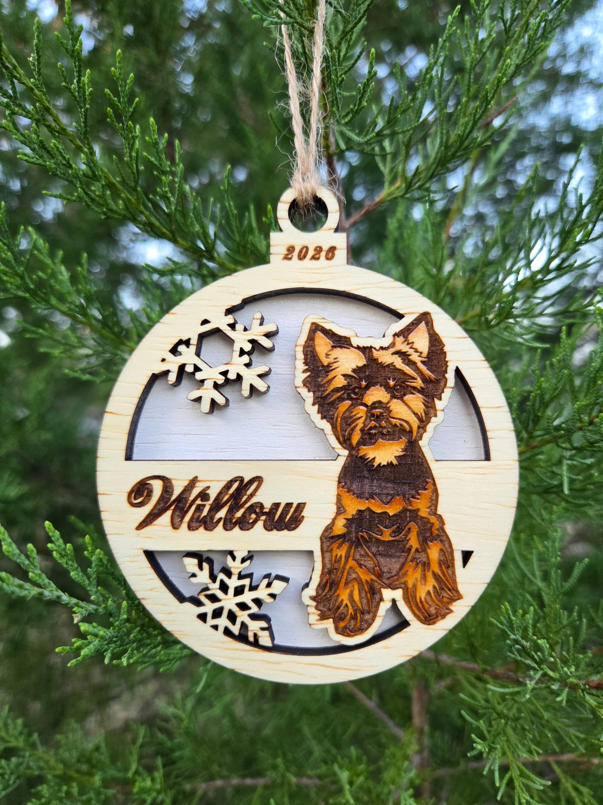 Yorkie and snowflakes ornament with a white back, engraved Willow and 2026, hanging on an evergreen