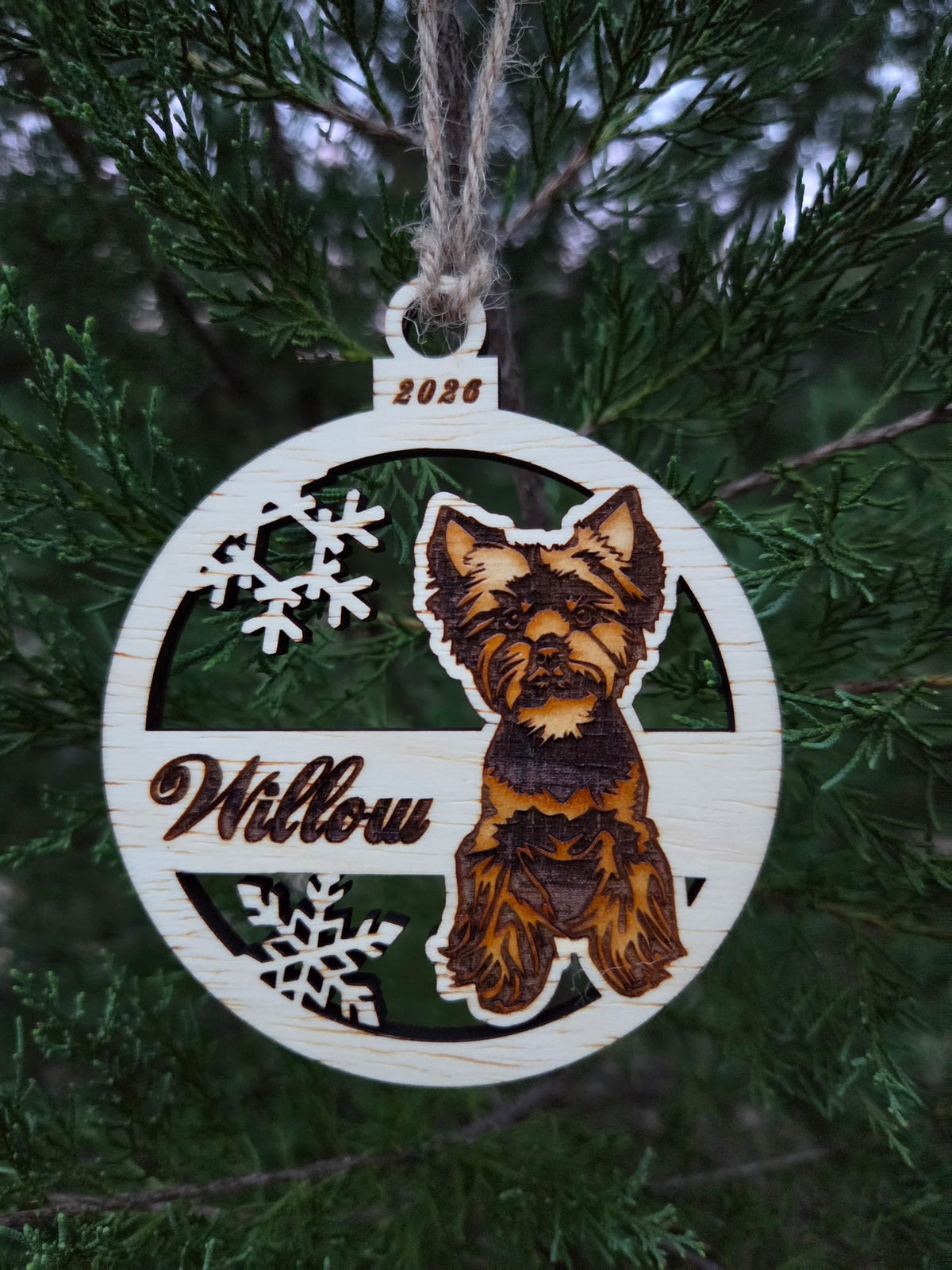Sitting Yorkie ornament hanging by its twine loop on an evergreen branch