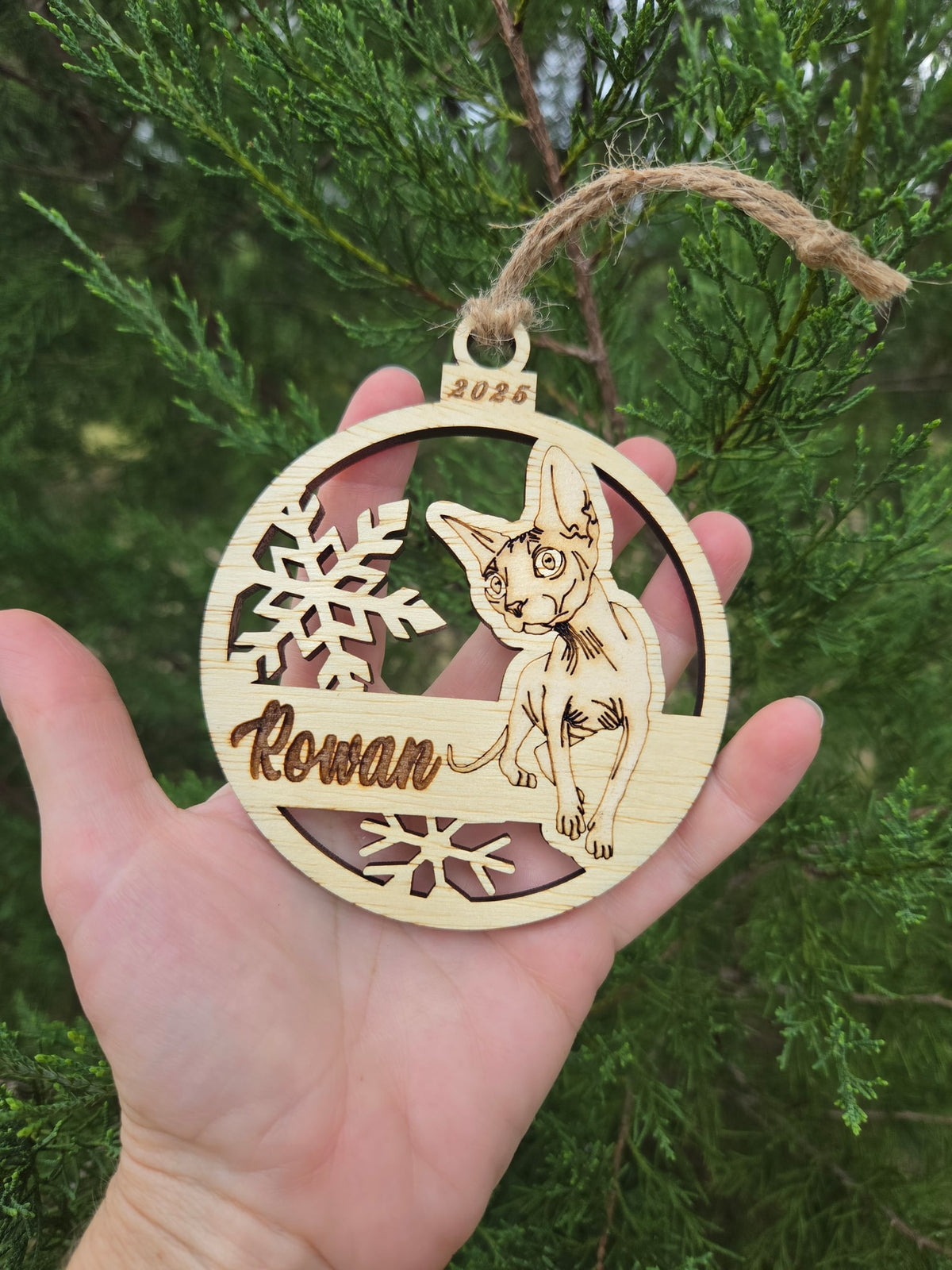 Sphynx cat and snowflakes ornament held in an open hand to show its size