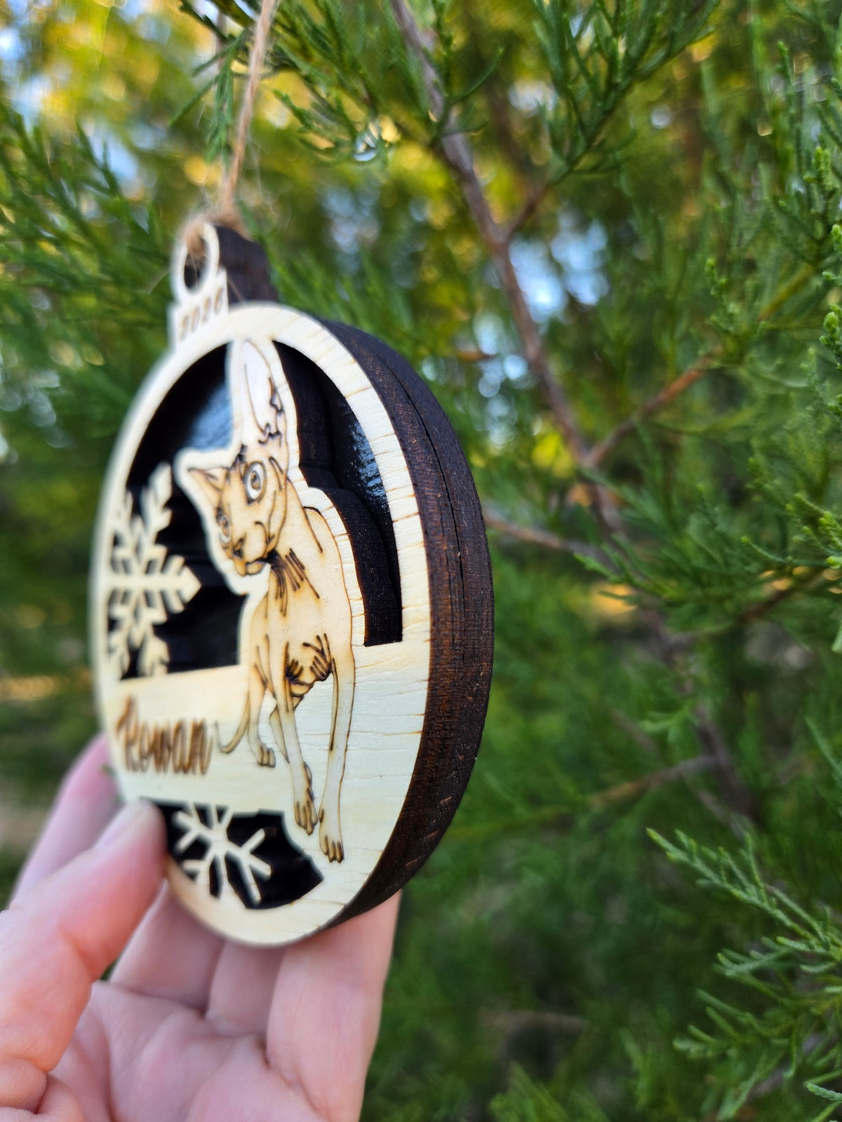 The Sphynx cat ornament with its black back, held in a hand to show its size