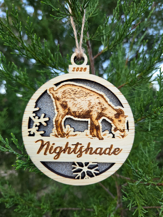 Standing goat and snowflakes ornament with a silver glitter back, engraved Nightshade and 2026, on an evergreen