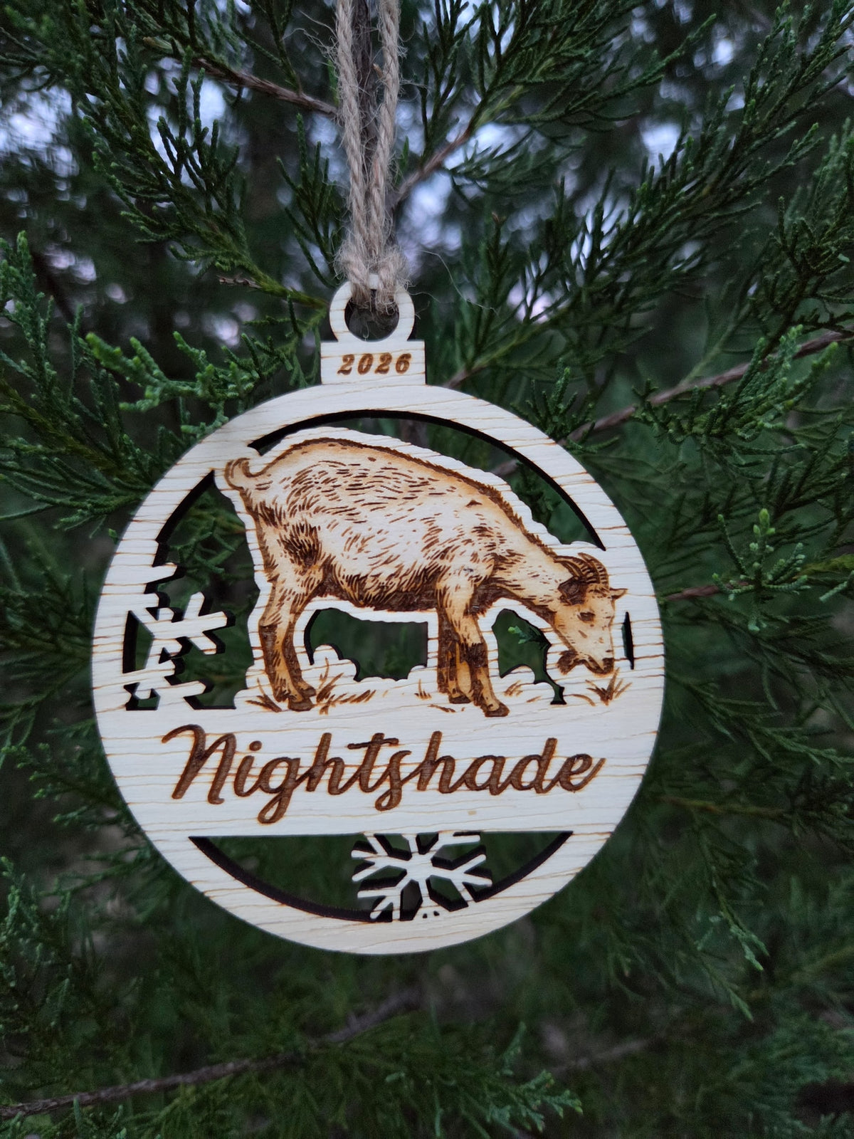 Standing goat ornament hanging by its twine loop on an evergreen branch