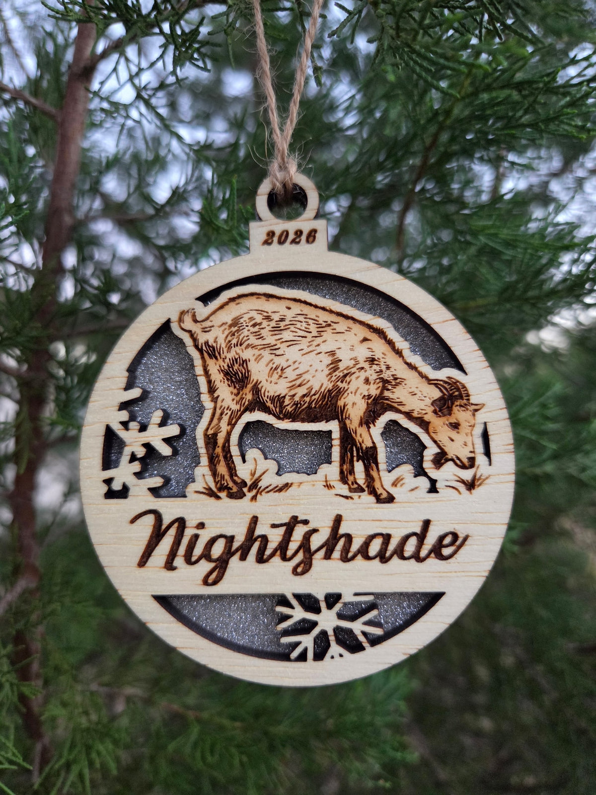 Standing goat ornament with a silver glitter back, engraved Nightshade and 2026, on an evergreen