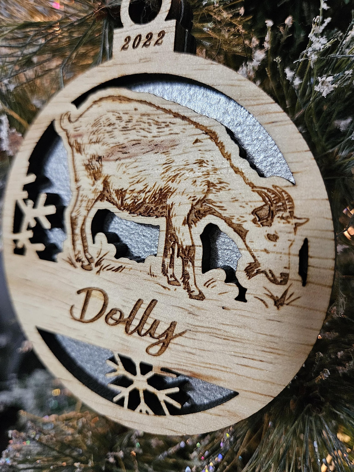 A finished standing goat ornament engraved Dolly, with a silver back, on a Christmas tree.