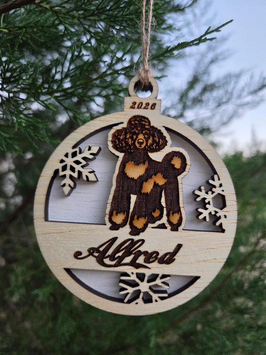 Round wooden standing poodle ornament with a white back, engraved Alfred and 2026, hanging on an evergreen branch
