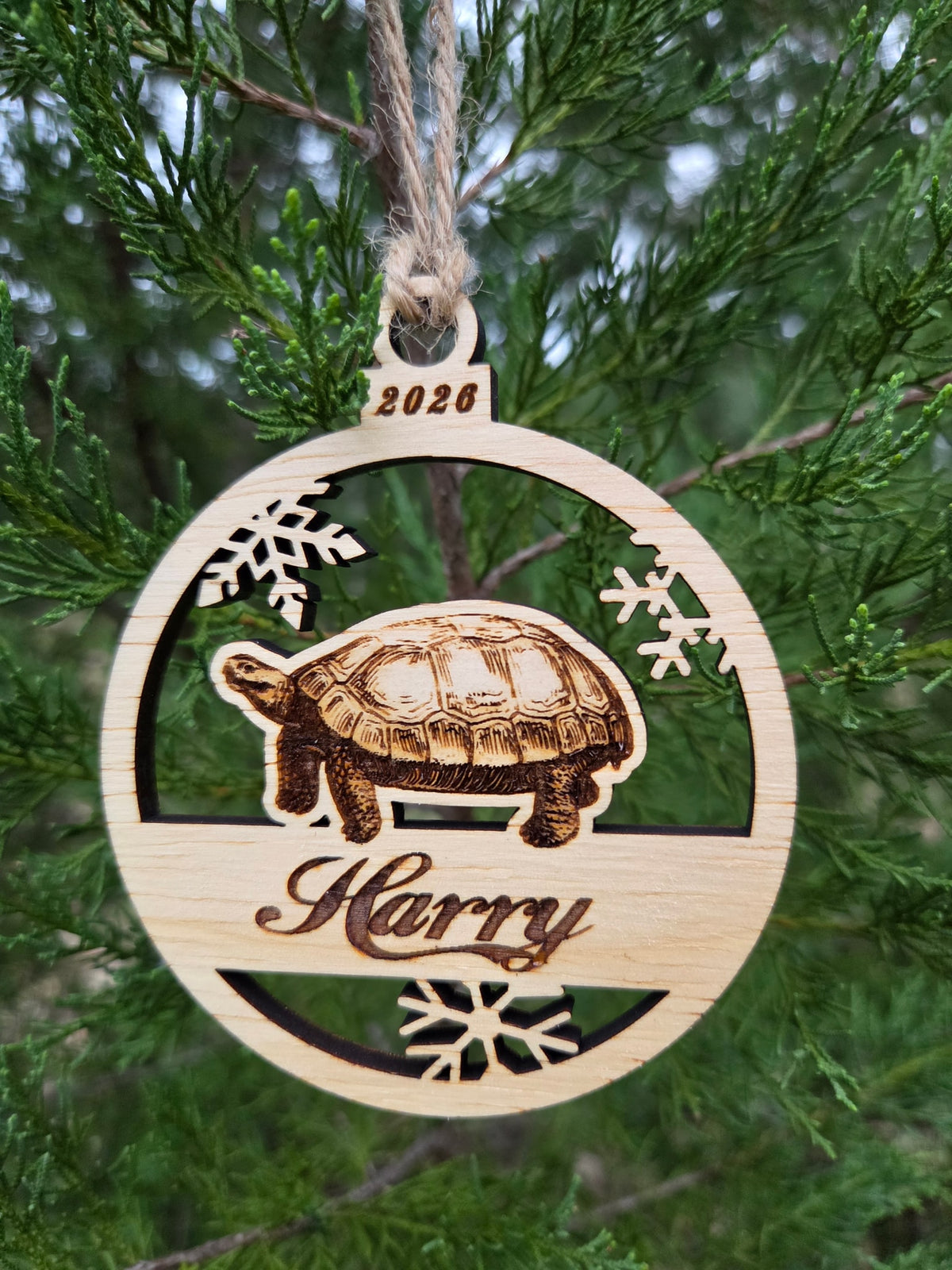 Tortoise and snowflakes ornament hanging by its twine loop on an evergreen branch