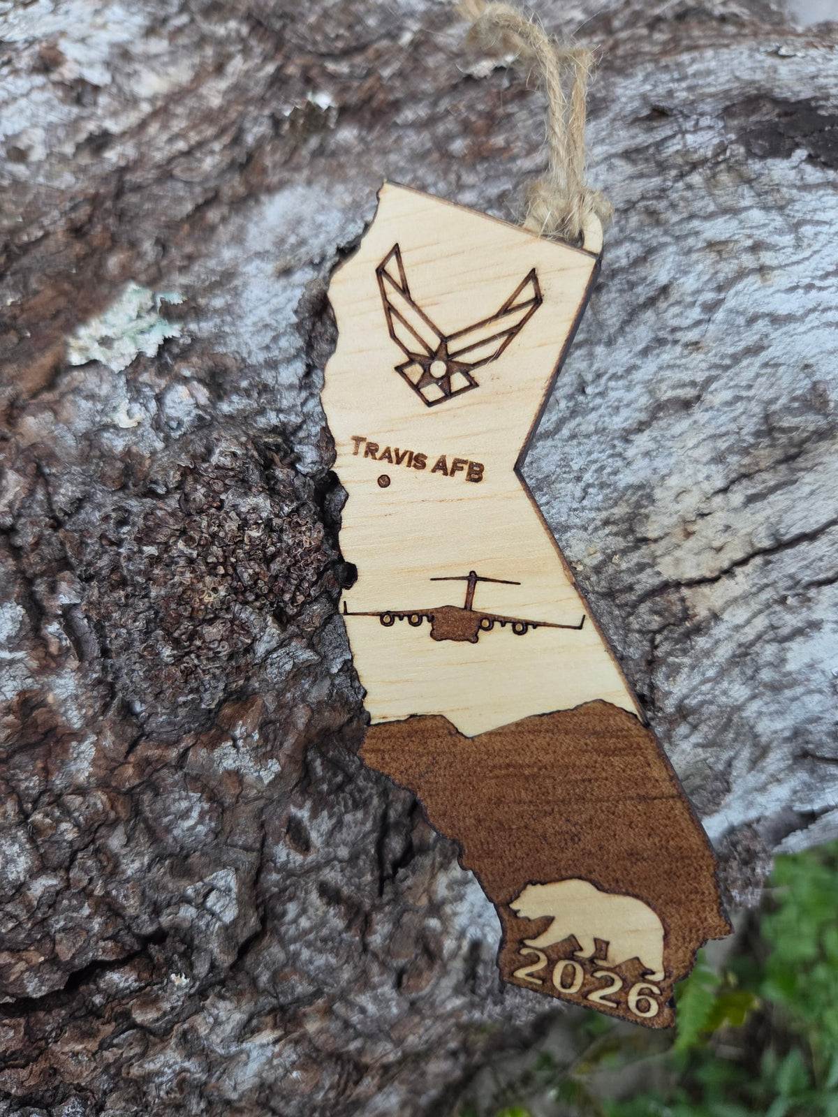 Travis AFB California ornament with its twine loop, resting on weathered tree bark