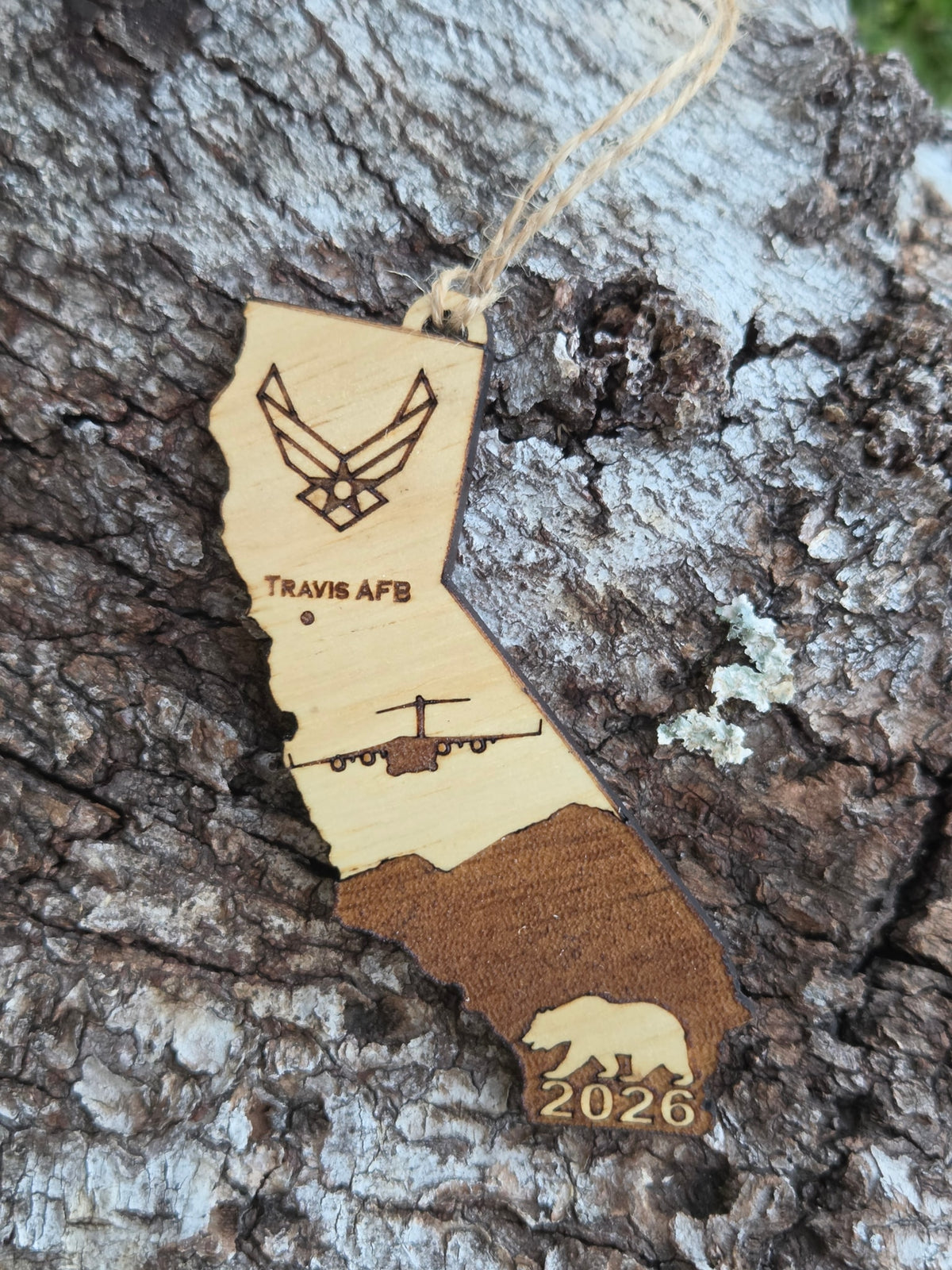 Travis AFB C-17 California ornament with its twine loop, resting on weathered tree bark