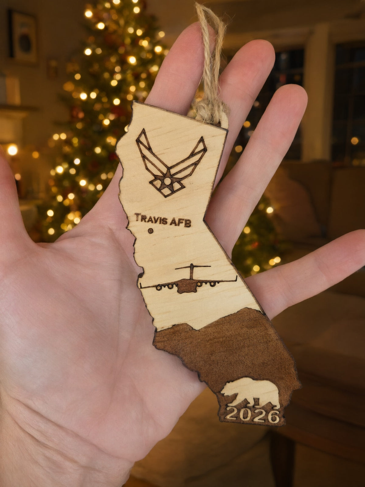Travis AFB California ornament held in an open hand in front of a lit Christmas tree