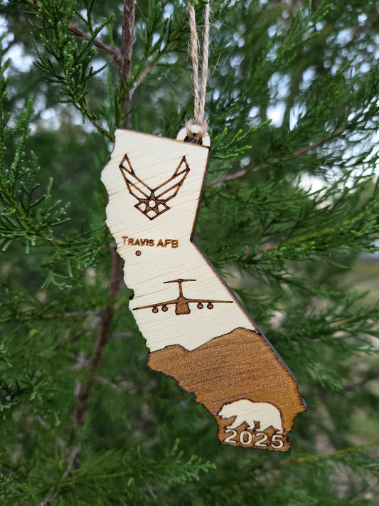 California-shaped wooden ornament engraved with Travis AFB, a C-5 and the year, hanging on an evergreen branch