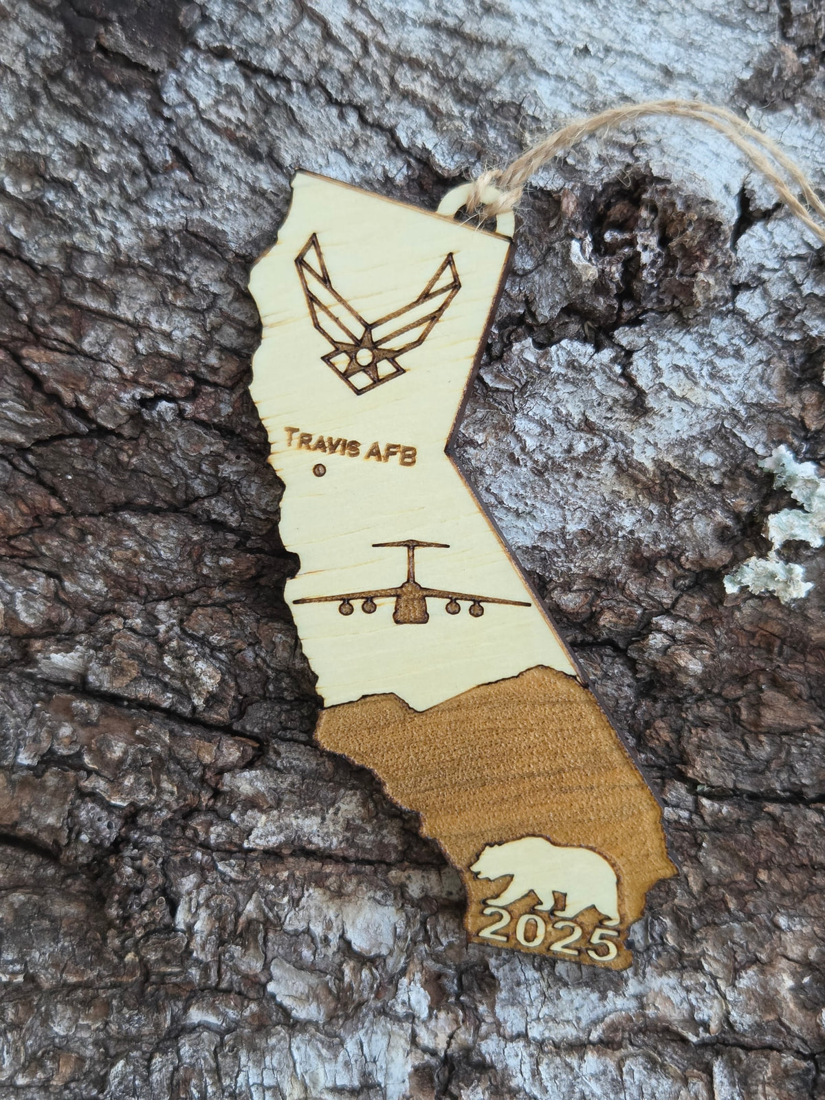 Travis AFB C-5 California ornament with its twine loop, resting on weathered tree bark
