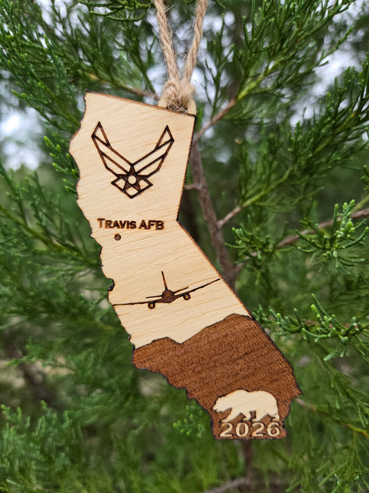 California-shaped wooden ornament engraved with Travis AFB, a KC-46A and the year, hanging on an evergreen branch