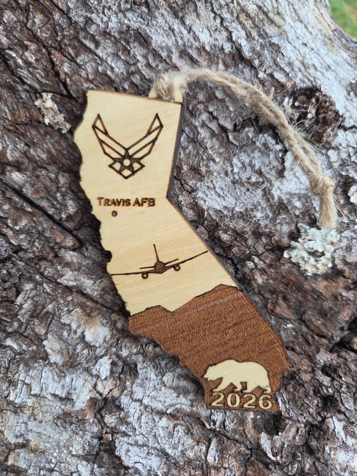 Travis AFB KC-46A California ornament with its twine loop, resting on weathered tree bark