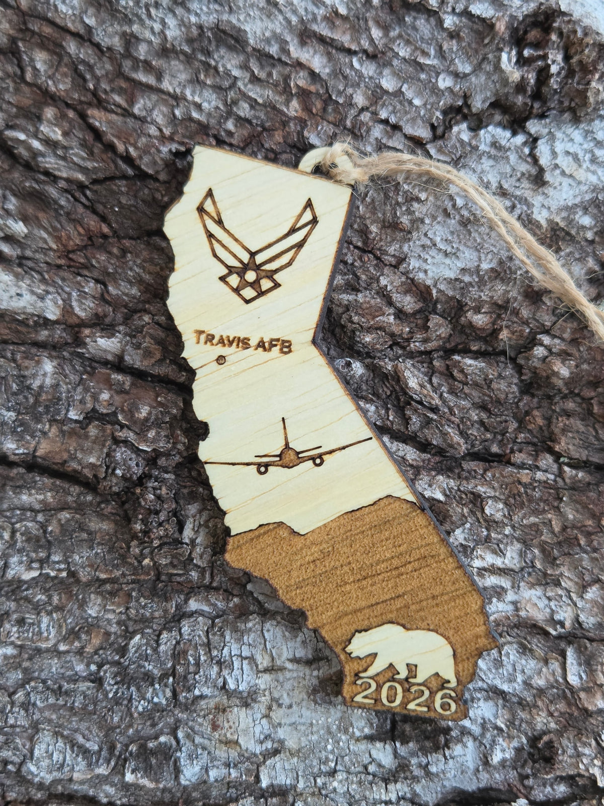 Travis AFB KC-46A California ornament with its twine loop, resting on tree bark
